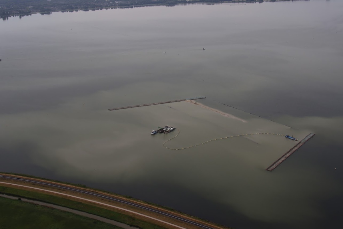 Je ziet een luchtfoto van boten die bezig zijn met de installatie van structuren op de bodem van het meer.